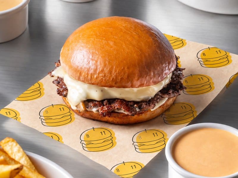 An 8-11 cheeseburger on branded paper with fries and two dips